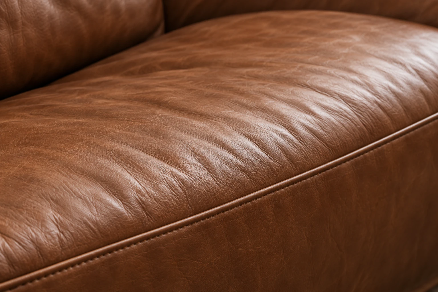Close view of a cognac leather seat cushion showing deep natural creasing across the sitting area and an intact welted edge