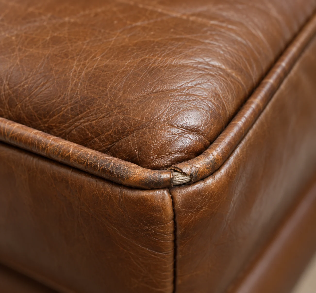 The corner of a cognac ottoman where the welt cord has worn through